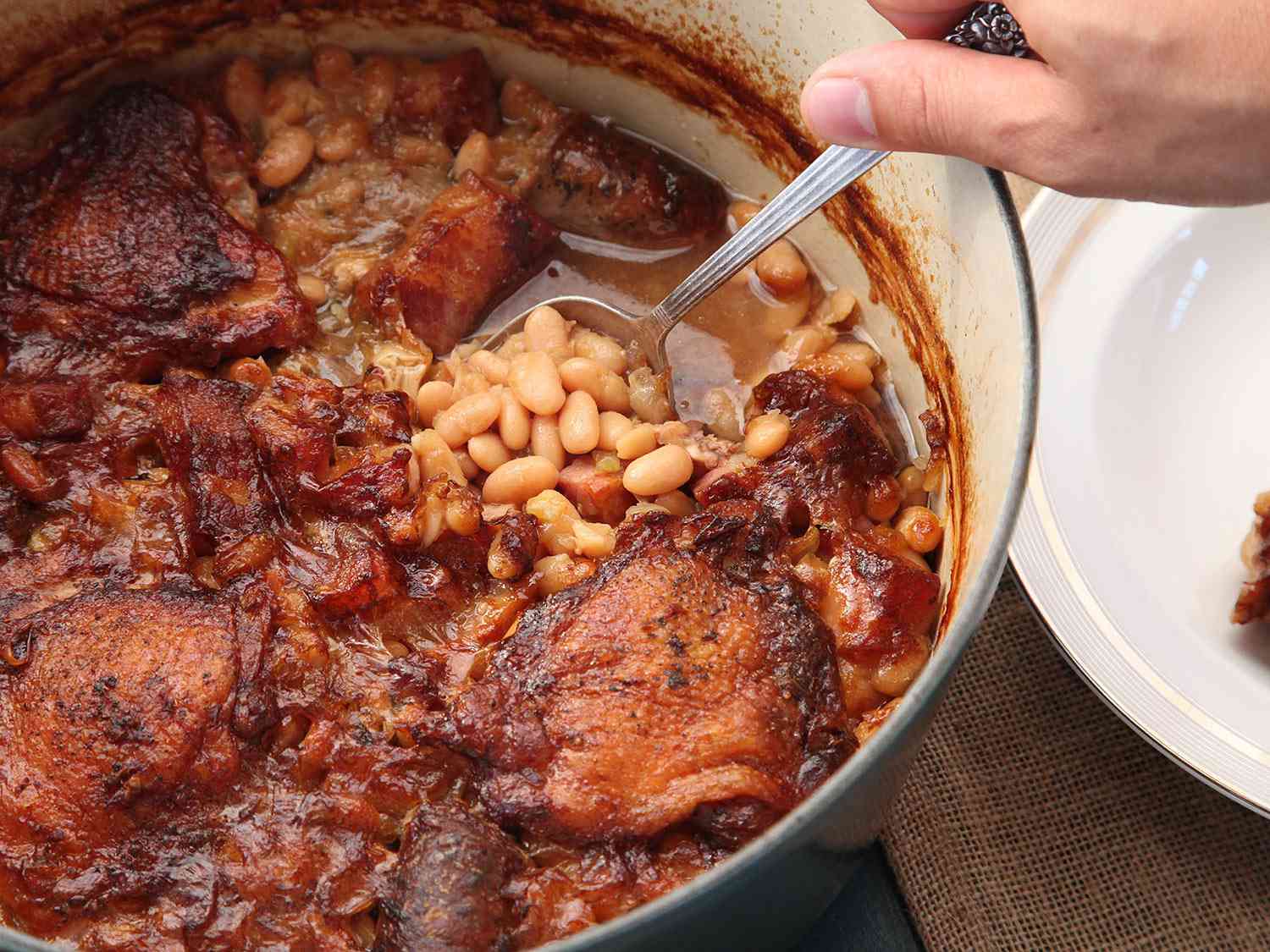 Scooping into a cassoulet baked in a Dutch oven with a crisp browned crust and creamy beans.