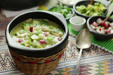 A bowl of green pozole verde topped with avocado and radish.