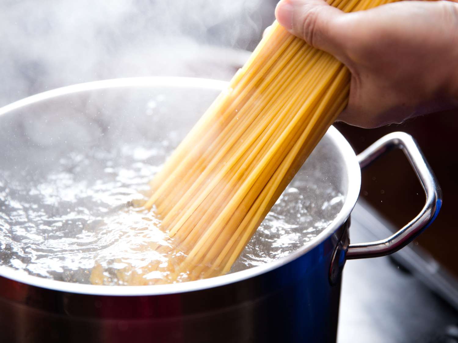 Close-up of dried bucatini being added to a pot of boiling water.