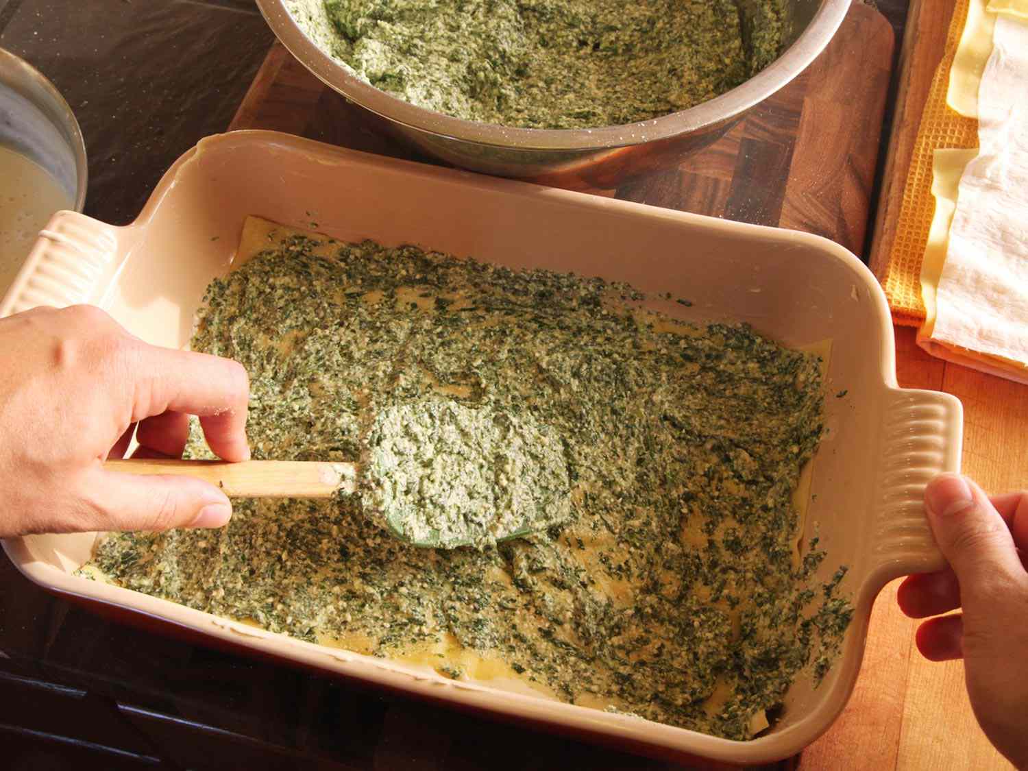 Laying down a thin layer of spinach mixture over pasta sheets