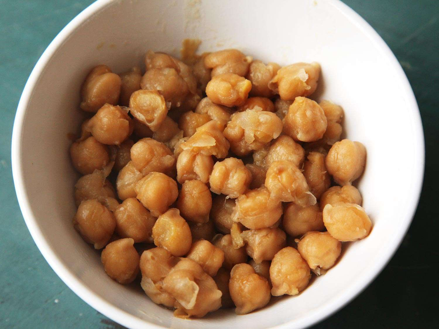 A white bowl of thoroughly cooked, falling-apart chickpeas