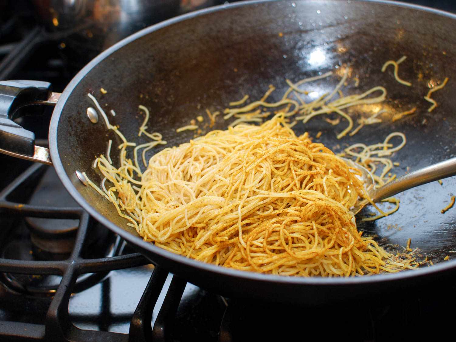 Spatula stirring curry powder into rice vermicelli noodles in a hot wok.