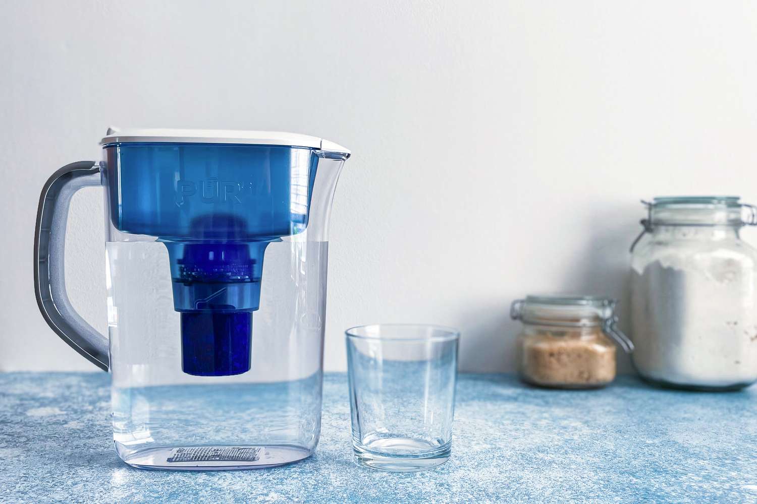 空玻璃杯旁边放着一个装满水的滤水罐
