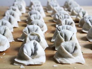 Array of uncooked wontons on a wooden cutting board.