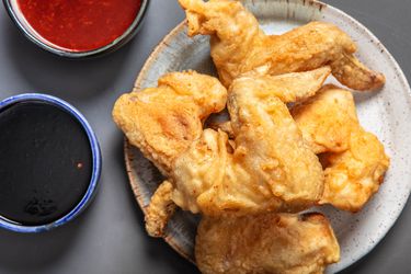 一个小板的韩国炸鸡翅和two dishes of sauce next to it.