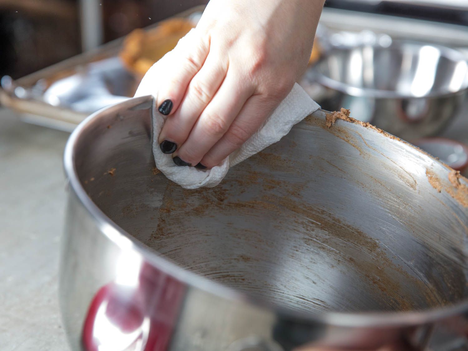 Wiping out the inside of a stand mixer bowl with a paper towel.