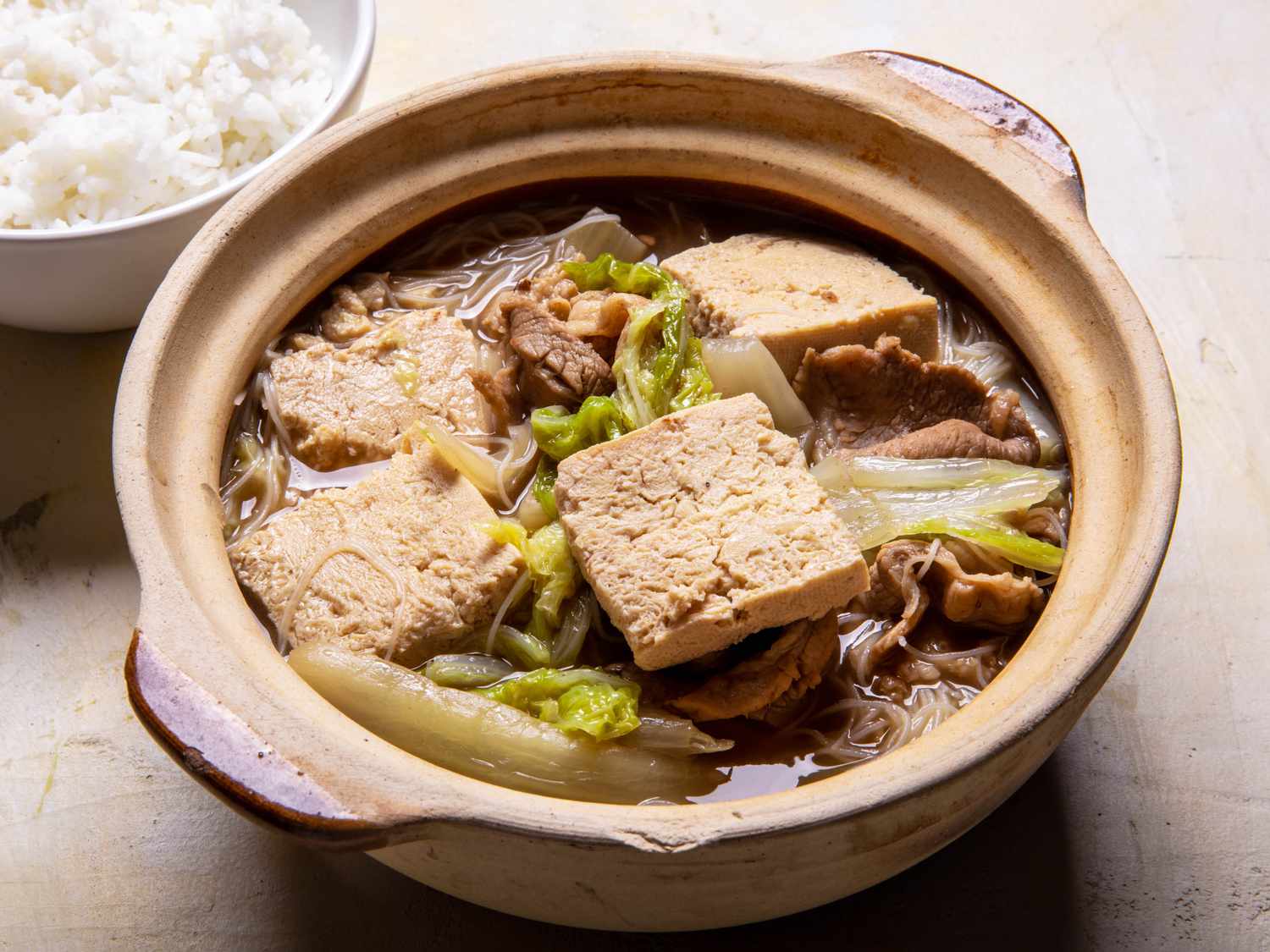 Serving bowl of Frozen Simmered Tofu Soup with Pork, Cabbage, and Rice Noodles with rice alongside