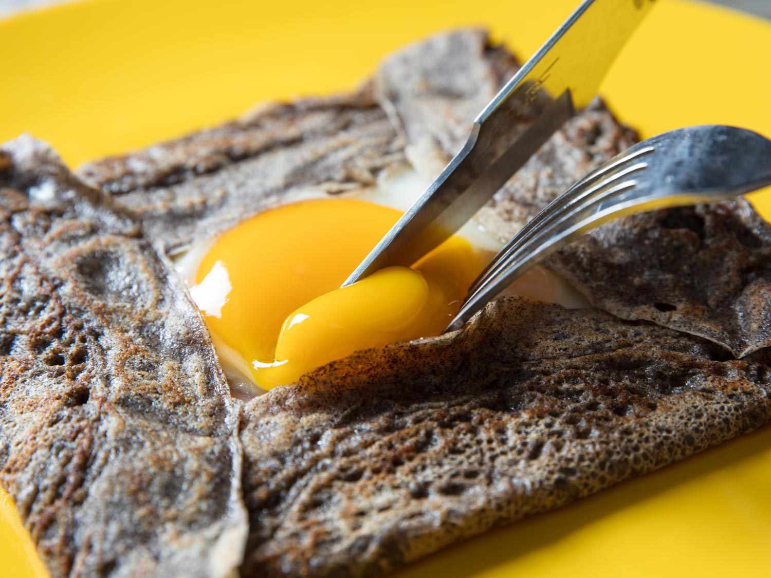 一个装满荞麦薄饼的特写。刀叉戳着露出来的单面鸡蛋的蛋黄。蛋黄还没有完全凝固，但它的糊状比松软多了。gydF4y2Ba