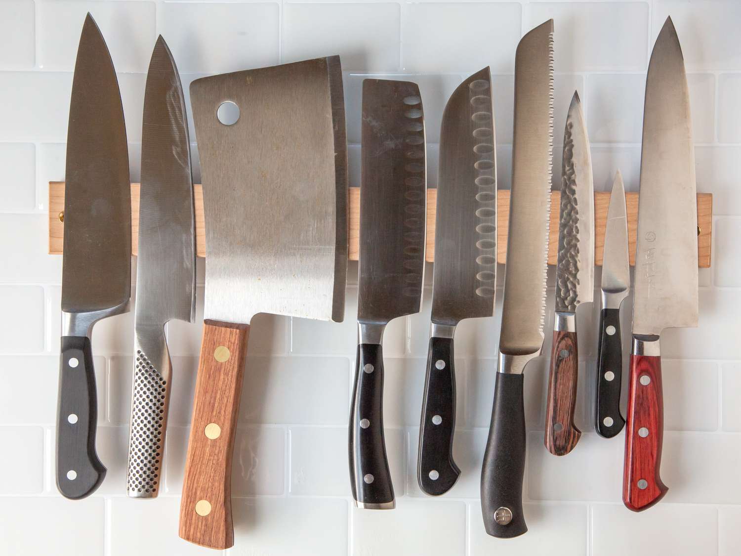 a variety of different knives hanging from a magnetic wooden knife holder