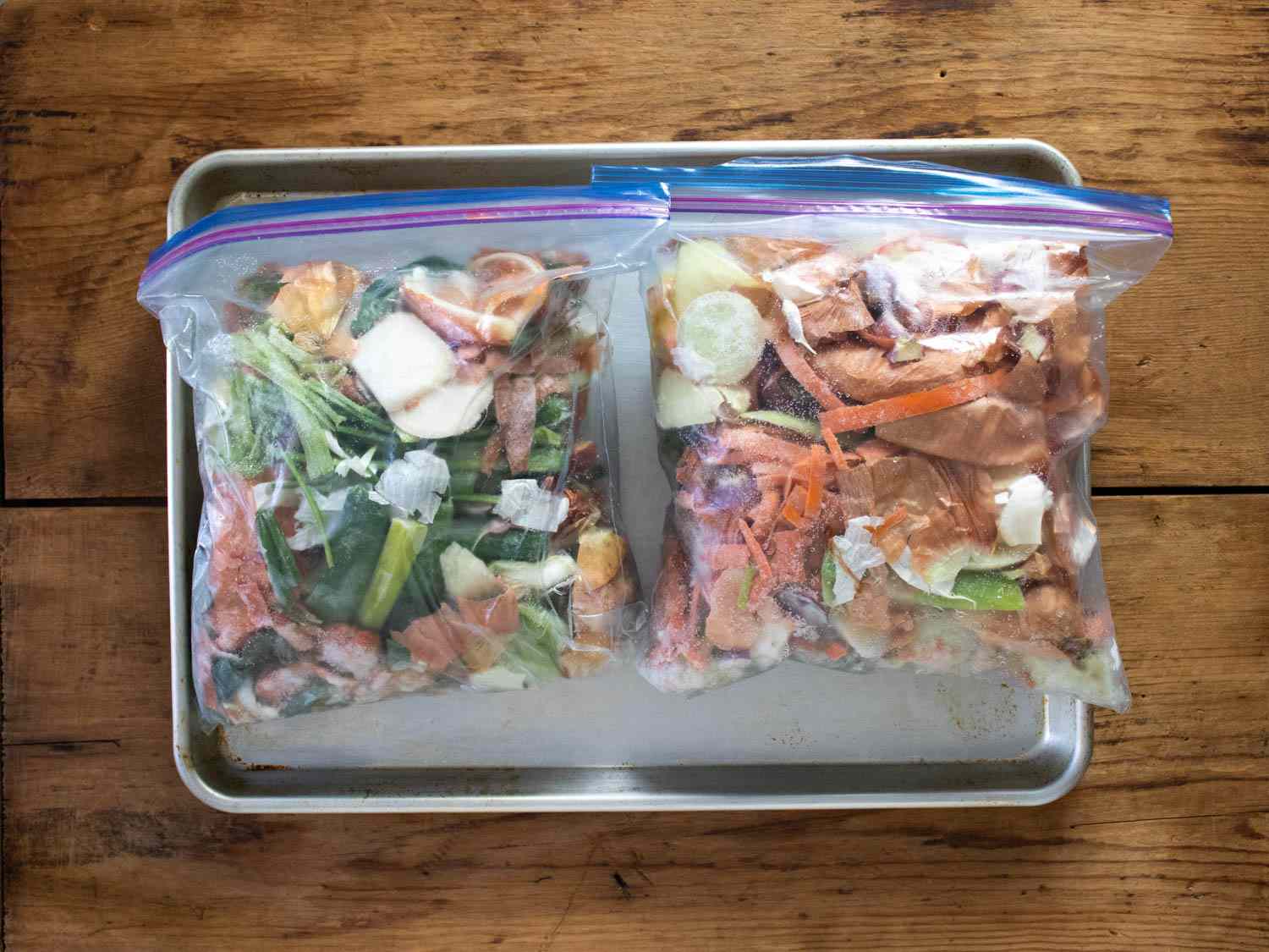 Two freezer bags filled with vegetable scraps on a sheet pan.