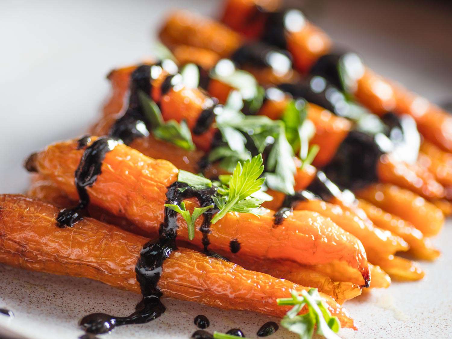 Closeup of roasted carrots drizzled with black sesame dressing and garnished with parsley leaves.