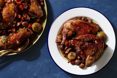 一种白色的蓝边盘子，盛着一大份葡萄酒烩鸡。在图片的左边是一个圆形的盘子，里面装着更多的酒焖鸡。