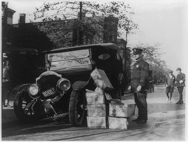 在一张黑白照片中，有几箱私酒和警察的破车