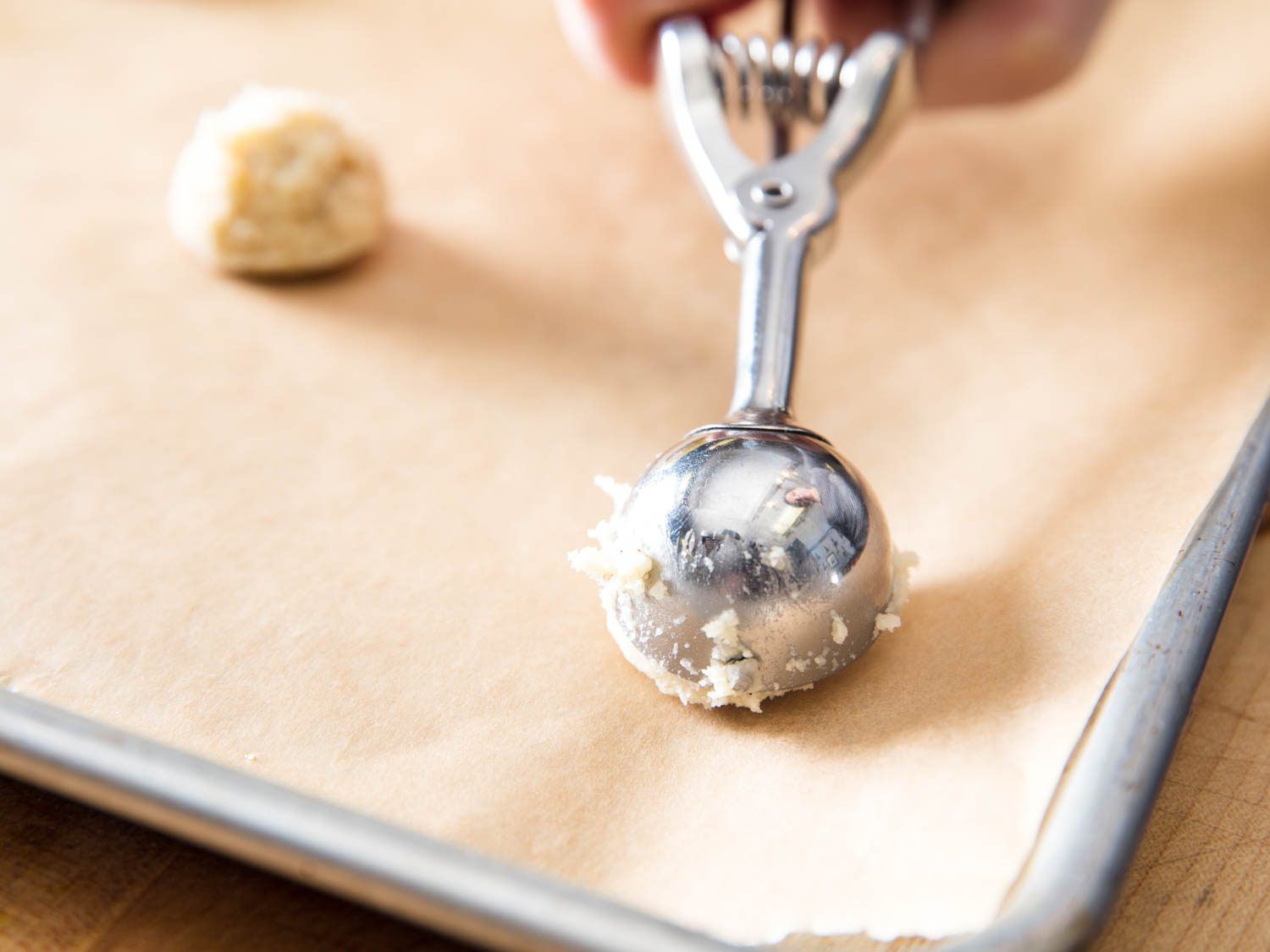 Cookie scoop portioning ricotta-brown butter cookie dough on parchment-lined baking sheet