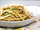 A shallow white bowl filled with a mound of pasta con sarde topped with bread crumbs.