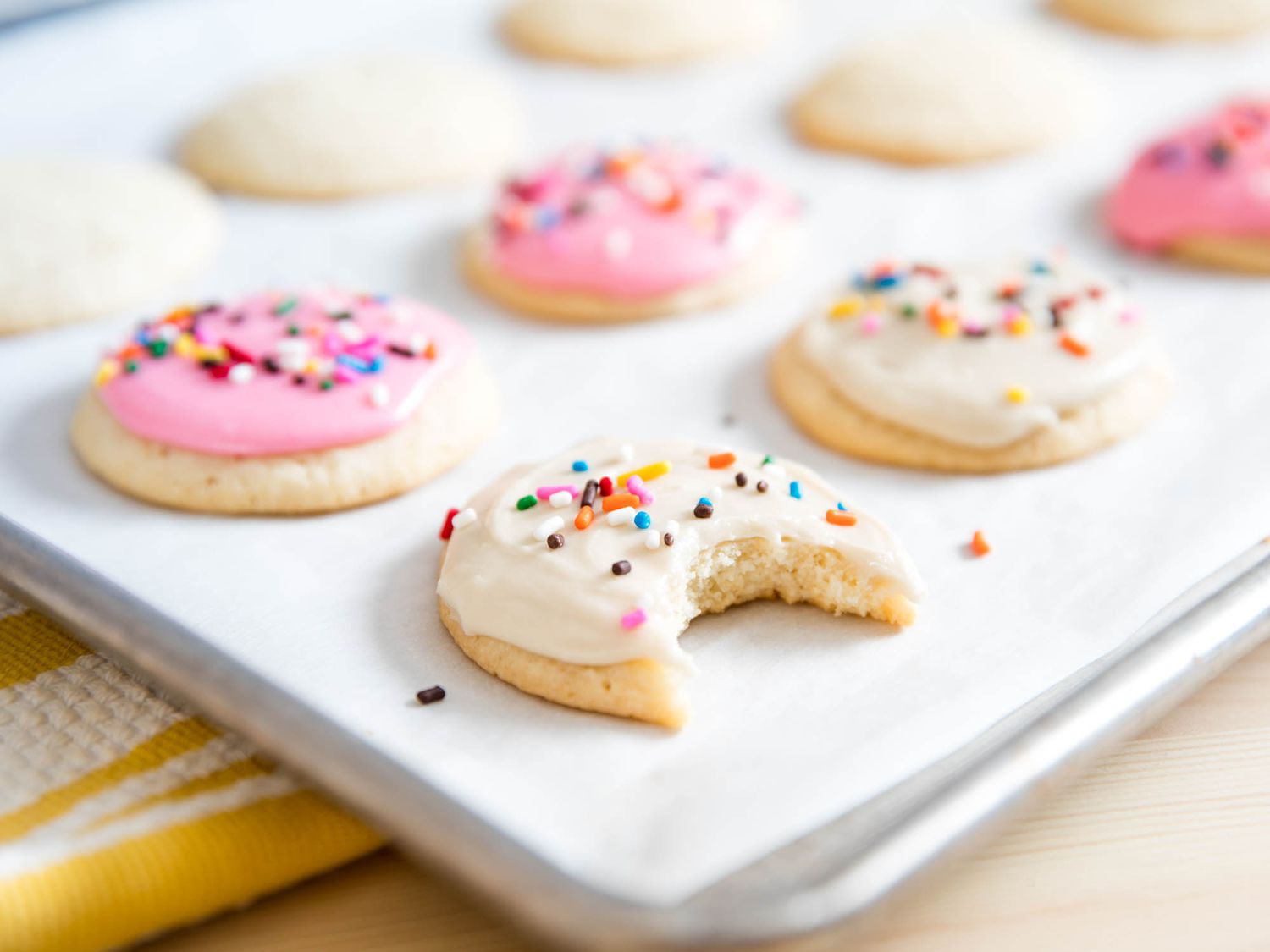White frosted cookies with sprinkles on a baking sheet