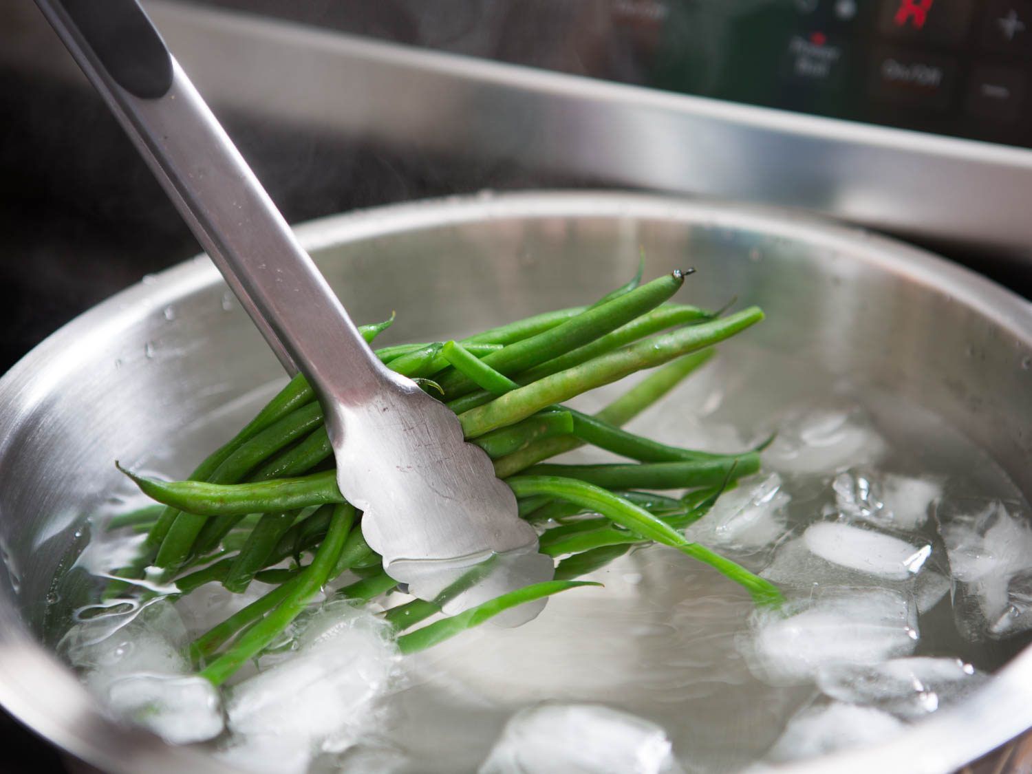 Using tongs to put boiled green beans in ice water.