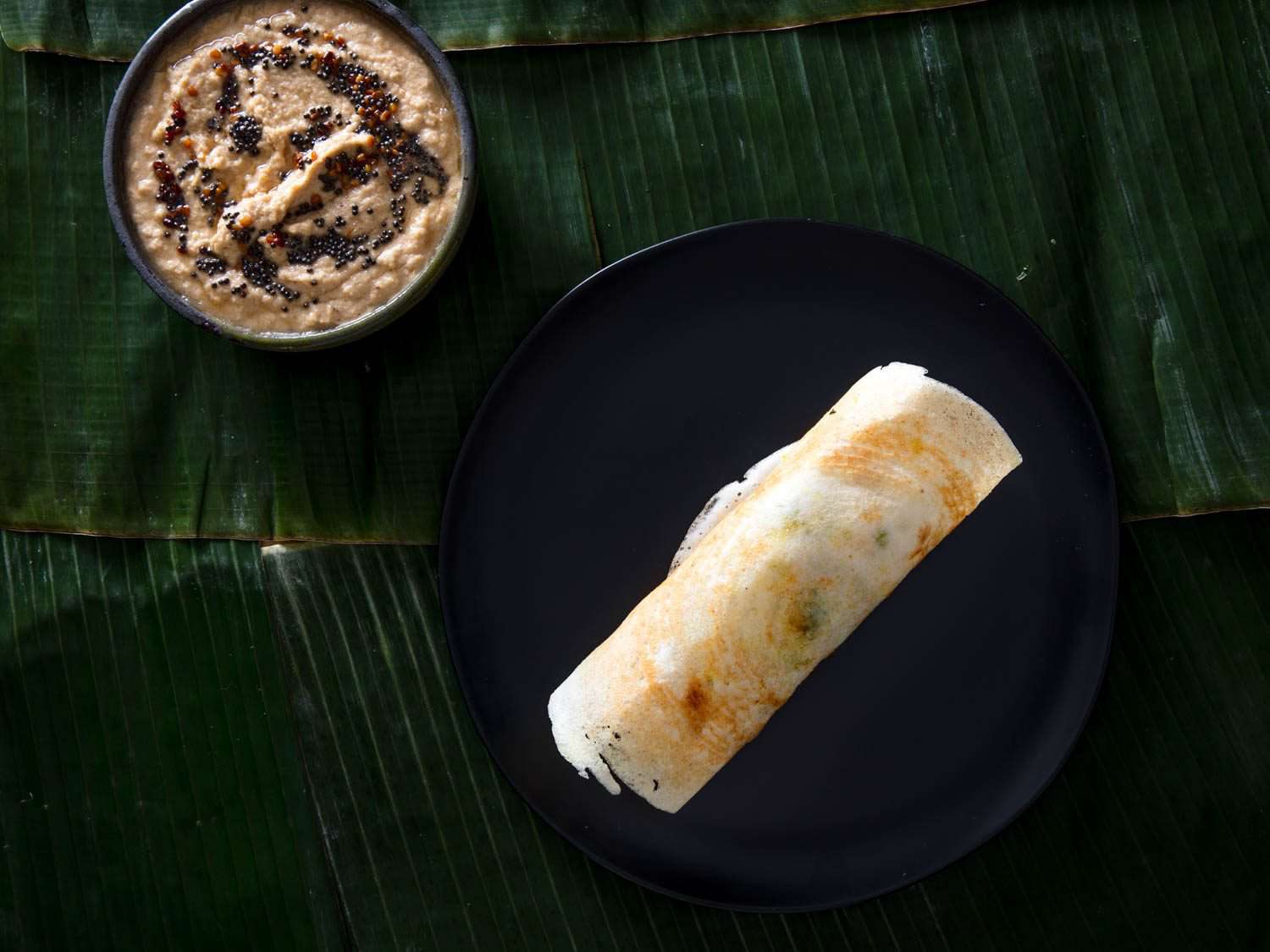 A dosa on a plate with a side of coconut chutney.