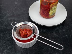 a small fine mesh strainer drains hot peppers of their oil