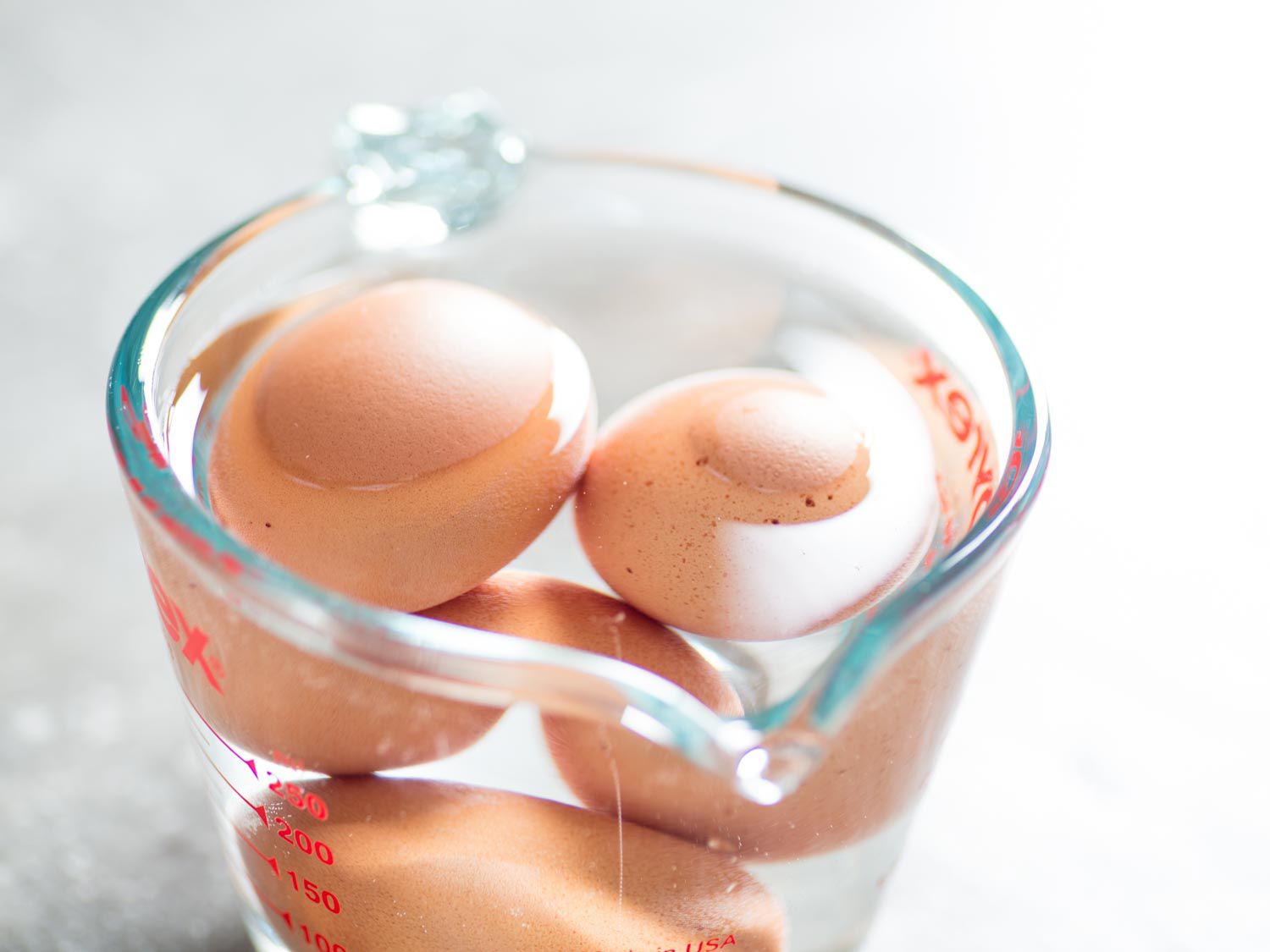 Brown eggs submerged in a measuring cup full of warm water.