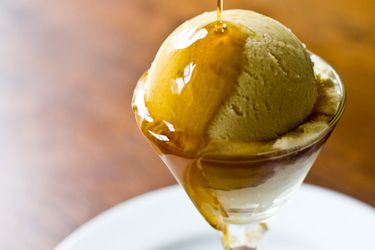 A scoop of maple ice cream in a coupe with maple syrup being drizzled on top.
