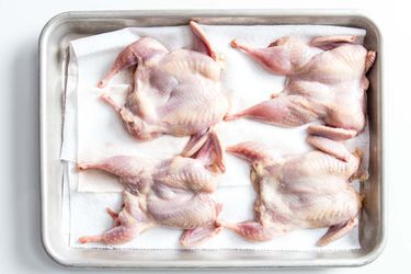 Overhead view of four quail placed on a paper towel-lined baking sheet. Two have been deboned; two have been spatchcocked.