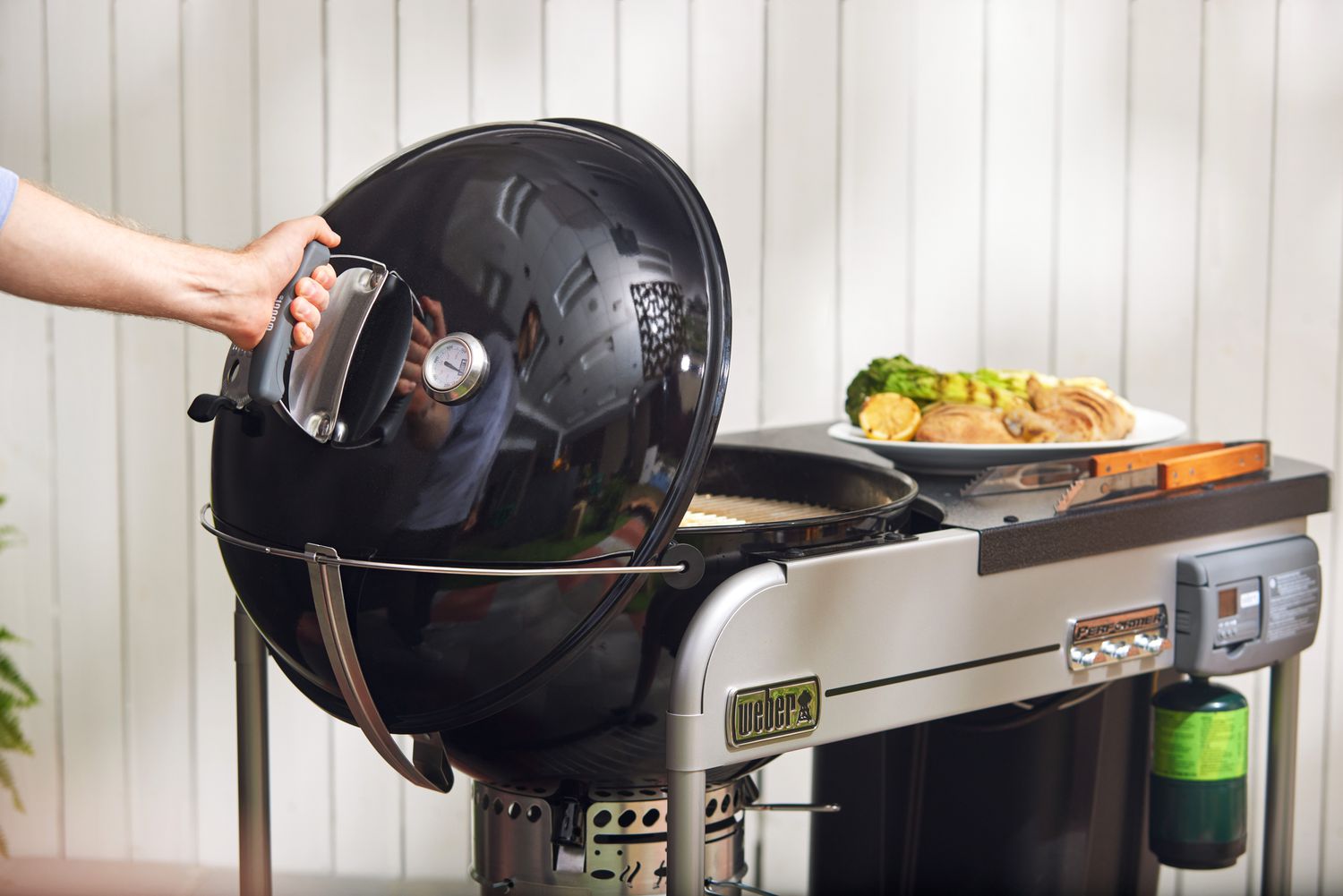 a person opening the lid of a charcoal grill