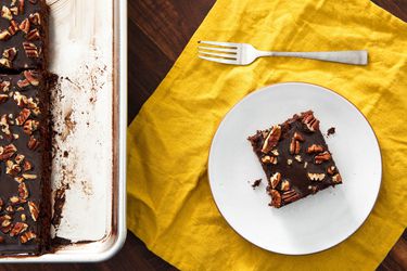 Overhead view of a slice of Texas sheet cake served on a white plate and set next to the rest of the cake.