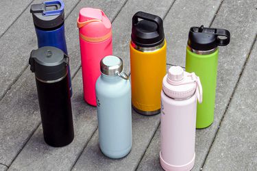 Seven stainless steel water bottles on a grey surface