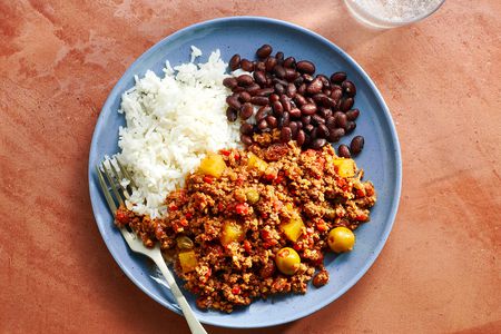 A blue ceramic plate with picadillo, white rice, and black beans.