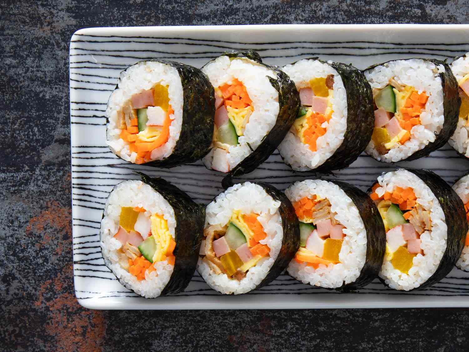 Overhead shot of two rows of sliced Korean kimbap rolls with colorful fillings.